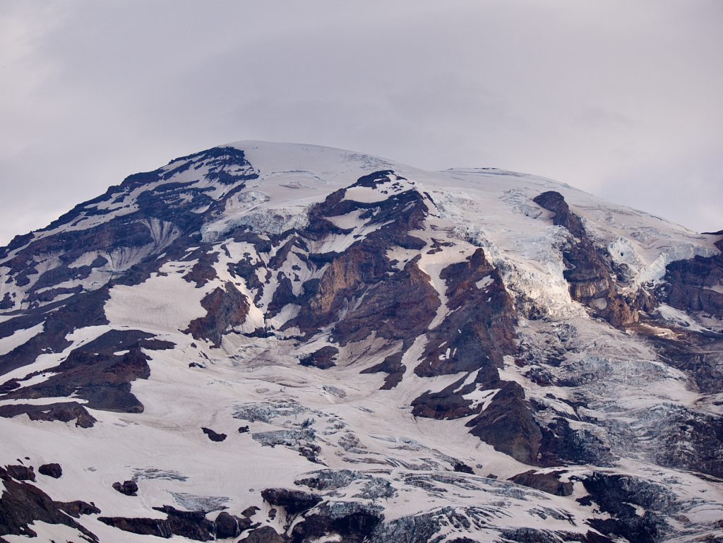 A beam of sunshine streaks across the southern side of Mount Rainier