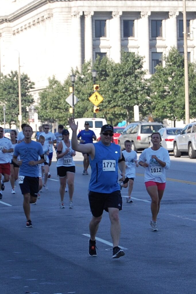 A white male waiving while running with a group of people.